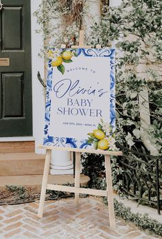 a baby shower sign sitting in front of a door with greenery on the side