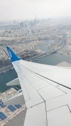 the wing of an airplane flying over a city and water area with buildings in the background