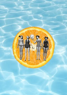 three women in swimsuits standing on top of an orange floating in the water