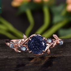 a blue diamond ring sitting on top of a piece of wood next to some flowers