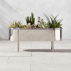 two metal planters with succulents in them on a tile floor next to a wall