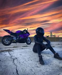 a person sitting on the ground next to a motorcycle with a sunset in the background