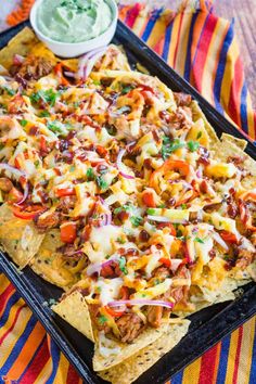 nachos on a tray with guacamole and salsa in the background