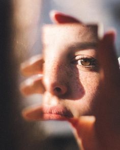 a close up of a person holding a cell phone to their face and looking in the mirror