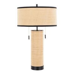 a table lamp with a black base and a beige shade on the top, sitting next to a white wall