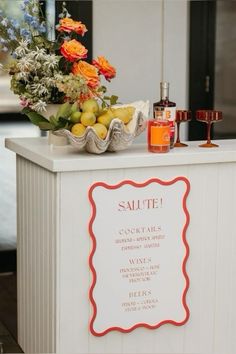 a sign that is sitting on top of a white counter with flowers and fruit in it