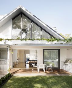 a white house with an open patio and dining area in the back yard is surrounded by greenery