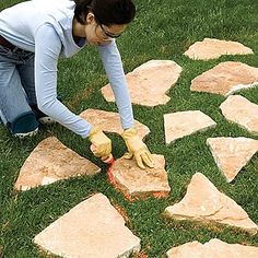 a woman in white shirt and yellow gloves painting rocks on grass