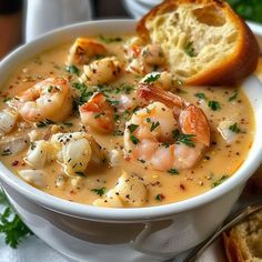 a bowl of soup with shrimp and bread on the side