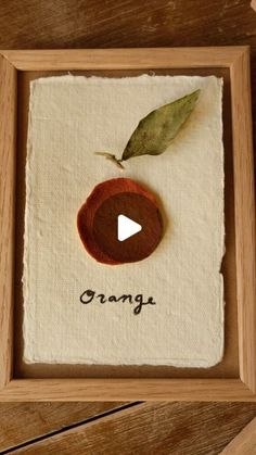 an orange is in a wooden frame with the word orange written on it and a green leaf