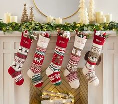 christmas stockings hanging from a mantel over a fireplace with candles and garland on it