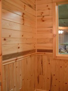 a bathroom with wood paneling and a window in the corner on the wall next to the toilet