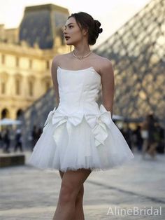 a woman in a short white dress is standing on the sidewalk and looking off into the distance