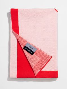 a pink and red blanket with a tag on it's side, sitting on top of a white surface