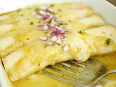 an enchilada in a white casserole dish with a fork resting on it