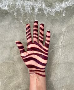 someone's hand painted with red and white stripes on the sand at the beach