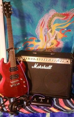 an electric guitar, amp and headphones are sitting on a colorful blanket next to a dragon wallpaper