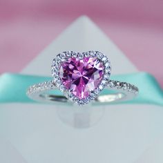 a pink heart shaped diamond ring on top of a white envelope