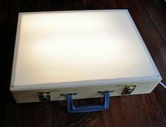 an open white suitcase sitting on top of a wooden floor next to a light bulb