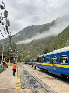 a blue and yellow train traveling down tracks next to a lush green mountain covered hillside