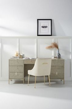 a white chair sitting in front of a desk next to a framed picture on the wall