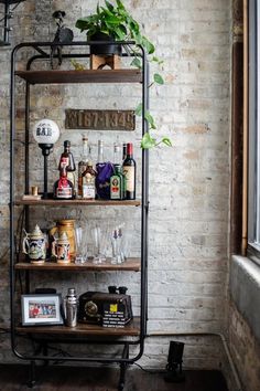 a shelf filled with bottles and glasses next to a window in a brick walled room