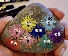 a hand holding a painted rock with flowers on it and eyes drawn on the rocks