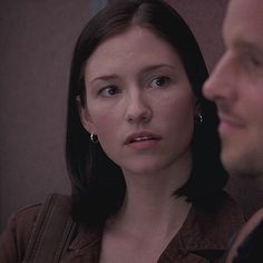 a woman standing next to a man in a brown shirt and earring necklaces