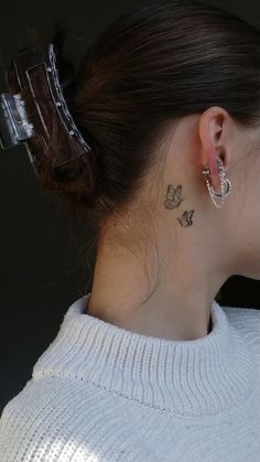 a woman with a butterfly tattoo on her left side behind the ear, wearing a white sweater