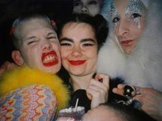 three people posing for a photo with clowns on their faces and one holding a drink