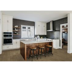 a large kitchen with white cabinets and wooden counter tops, along with two stools at the island