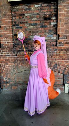 a woman dressed as a princess holding a raccoon in front of a brick wall