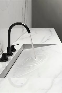 a black faucet running water from a sink in a white marbled bathroom