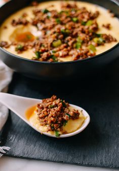 a bowl filled with food next to a spoon on top of a black tablecloth