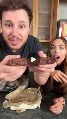 a man and woman are looking at a chocolate sandwich in front of the camera,