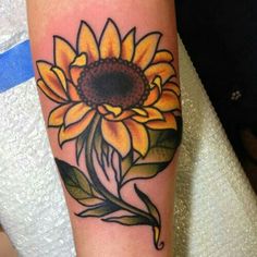 a sunflower tattoo on the arm with leaves and petals around it's center