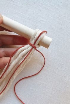 someone is holding a piece of white yarn with red thread on it and pulling the ends together