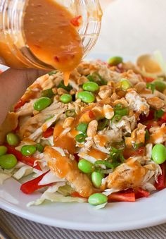 someone is pouring dressing onto a salad on a white plate with peas and carrots