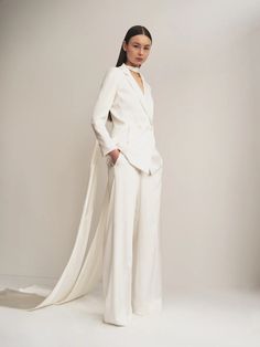 a woman standing in front of a white backdrop wearing a suit and long shawl