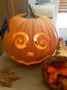 a carved pumpkin sitting on top of a counter next to a basket filled with carrots