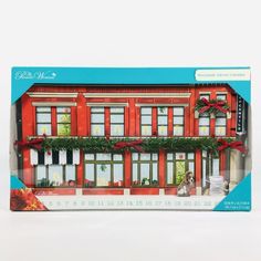 a red building with lots of windows and plants on the front is in a box