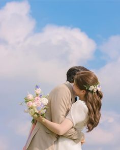 a bride and groom kissing in front of a blue sky with white clouds behind them