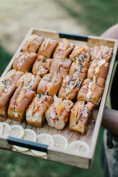 a person holding a wooden tray filled with sandwiches