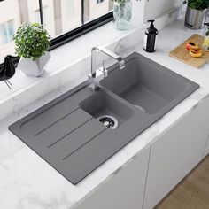 a kitchen sink sitting on top of a white counter next to a potted plant