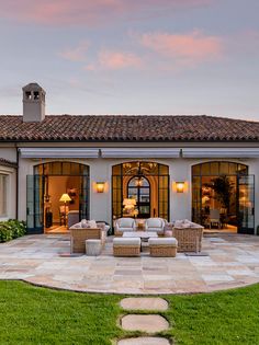 a patio with chairs and tables in front of a large house at sunset or dawn