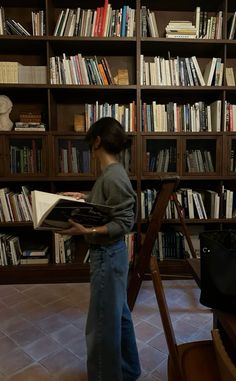 a person standing in front of a bookshelf holding a book and looking at it