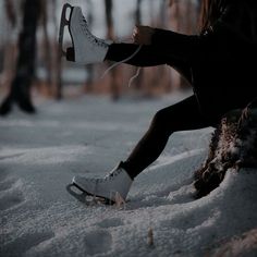 a person sitting in the snow with their feet up on a tree stump and wearing white tennis shoes