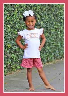 Prepare for baseball season in style with our Baseball Smocked Red Plaid Short Set. The white knit shirt features smocked bats and baseballs, creating a playful and sporty look with girly red picot trim on the angel sleeves. Paired with red gingham plaid shorts, this coordinated set strikes the perfect balance between style and comfort.childrens clothing, baseball season, baseball smocking, gingham outfit, red gingham, baseball bat and ball, bubble, jon jon, short set, dress, ruffles, little girls baseball outfit, little boys baseball outfit, mlb, mlb game, mlb gameday ootd, spring training outfit, play ball, kids mlb game outfit, red baseball teams, southern sunshine, kids playwear, classic whimsy, smocked auction, Dallas Texas, online shopping, kids clothing collection, summer baseball