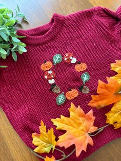 a knitted sweater with buttons and leaves on the table next to it is a potted plant