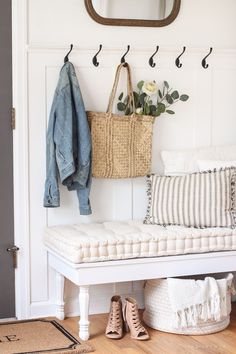 a white bench with some shoes on it and a basket hanging from the wall next to it